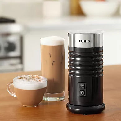 Black Keurig coffee maker on a wooden surface with a glass of iced coffee and a cup of hot coffee.