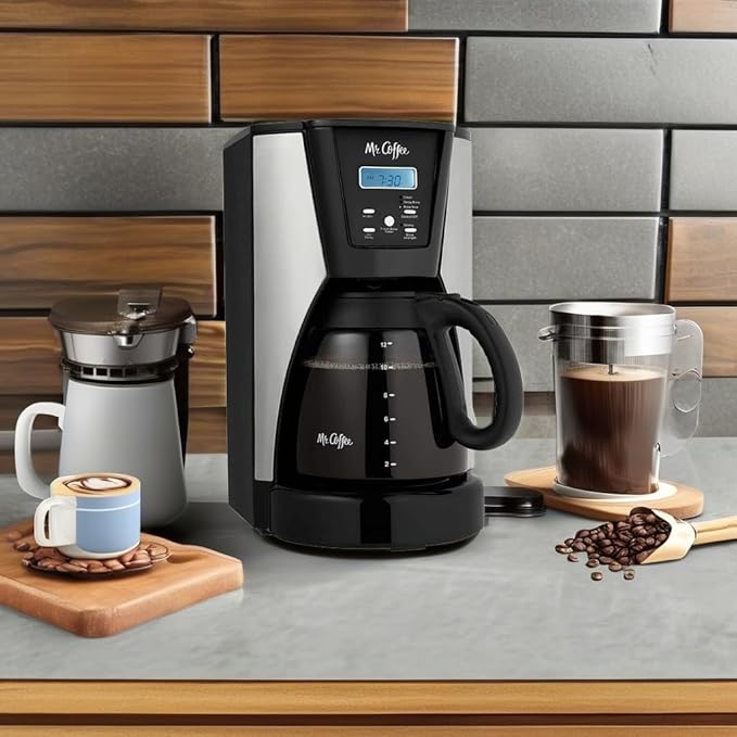 Black coffee maker on a kitchen counter with coffee cups, beans, and a tiled wall background.