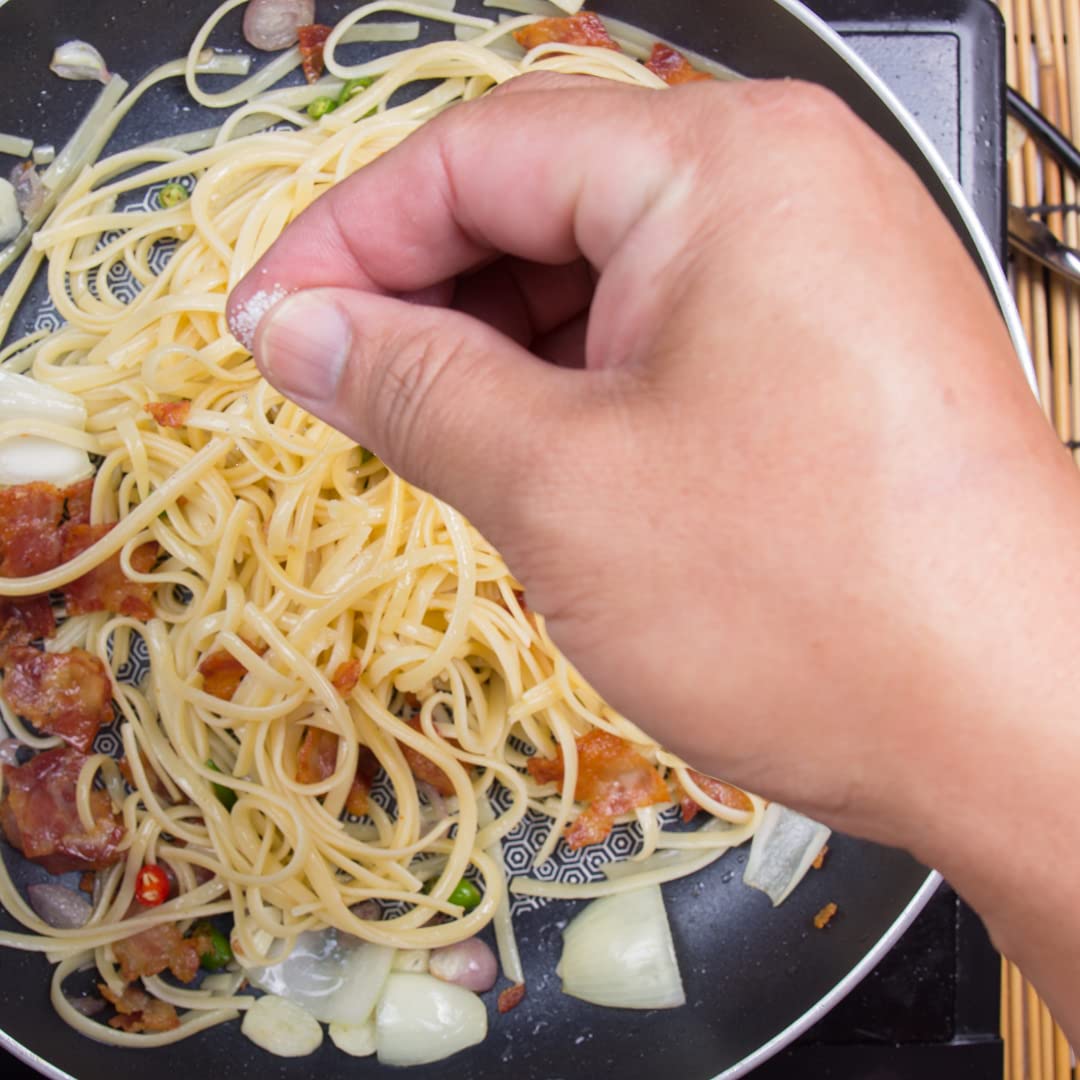 Hand stirring spaghetti with vegetables in a pan
