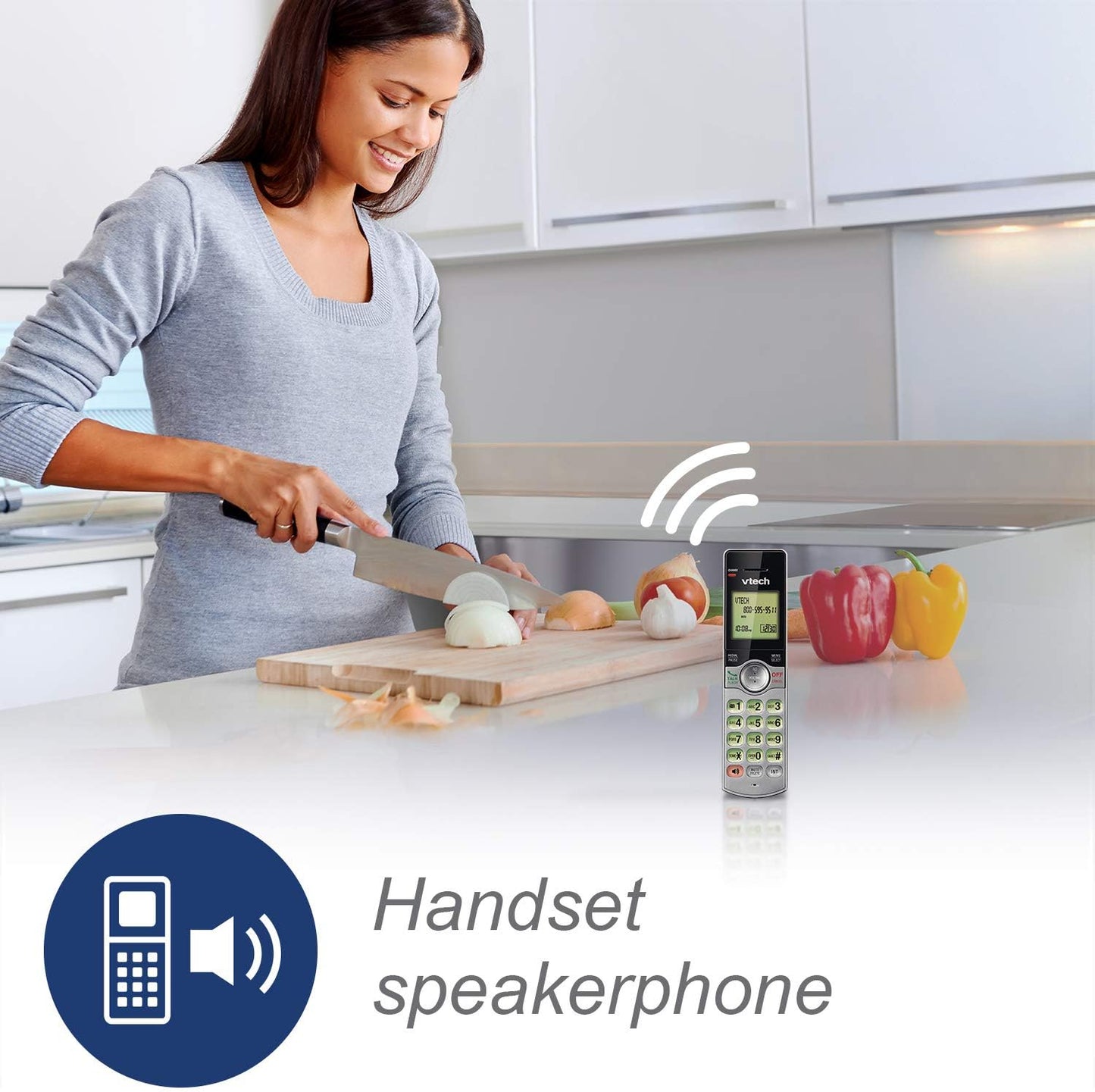 Woman in kitchen using a handheld speakerphone, with vegetables on the counter.