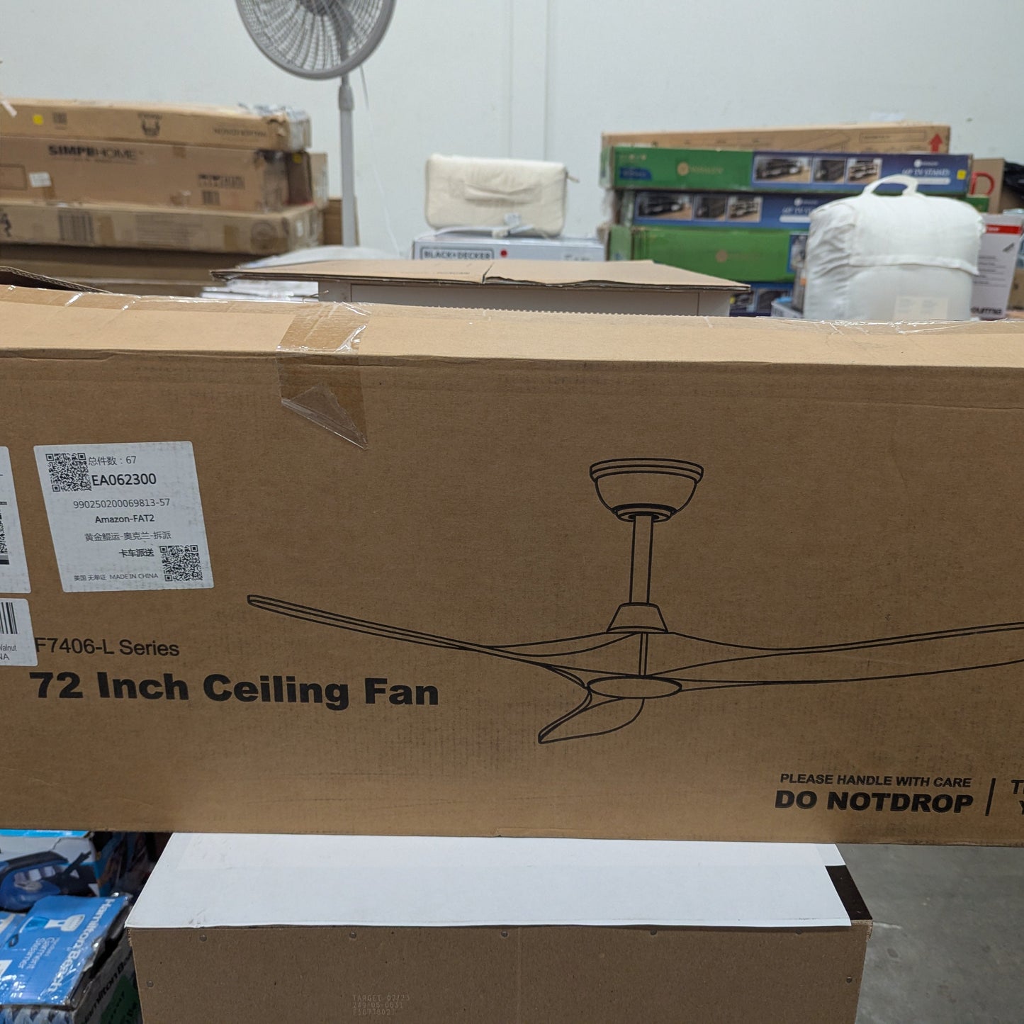 Cardboard box with a ceiling fan design and text, placed on a concrete floor with boxes and a fan in the background.