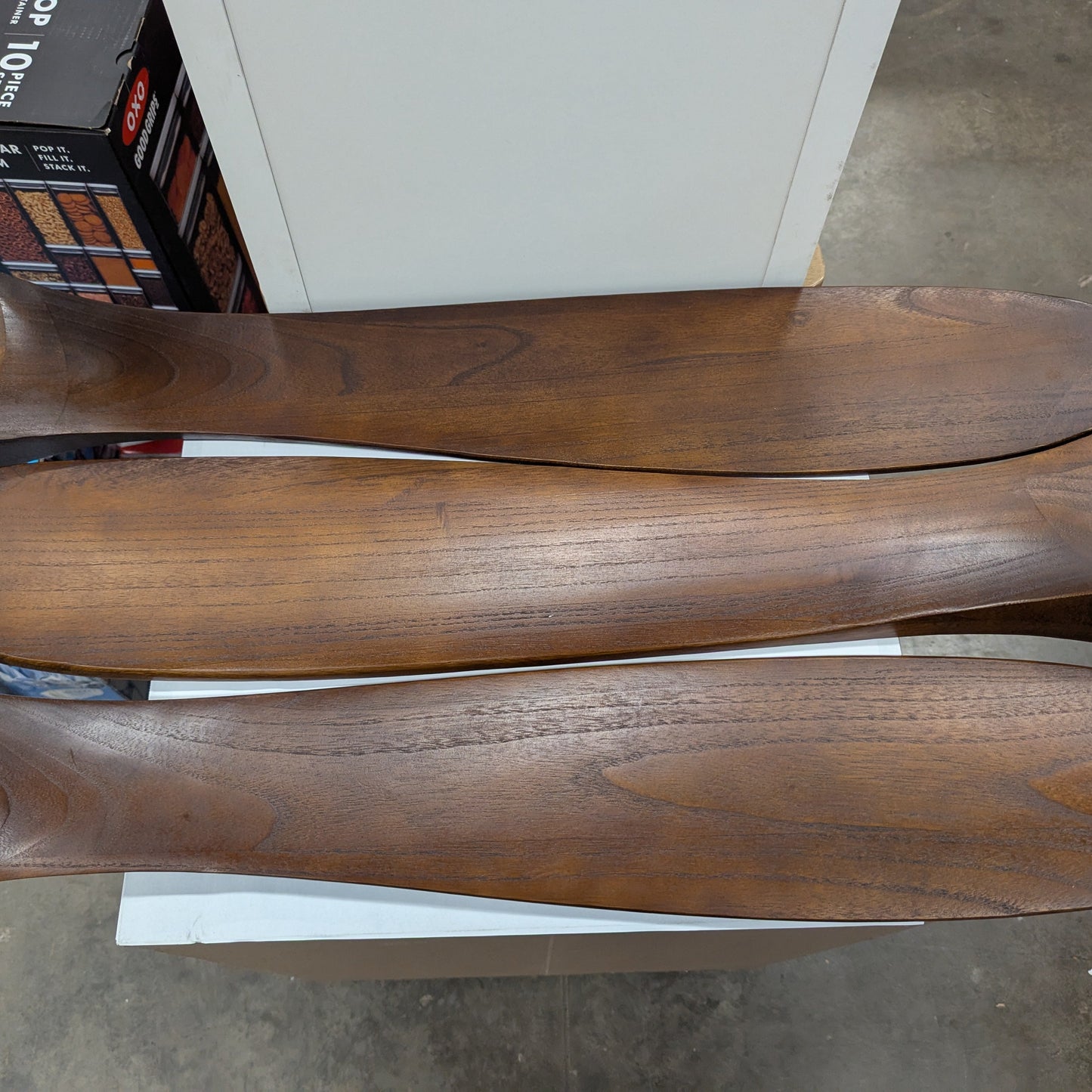 Three wooden shoe trees on a concrete floor with boxes in the background