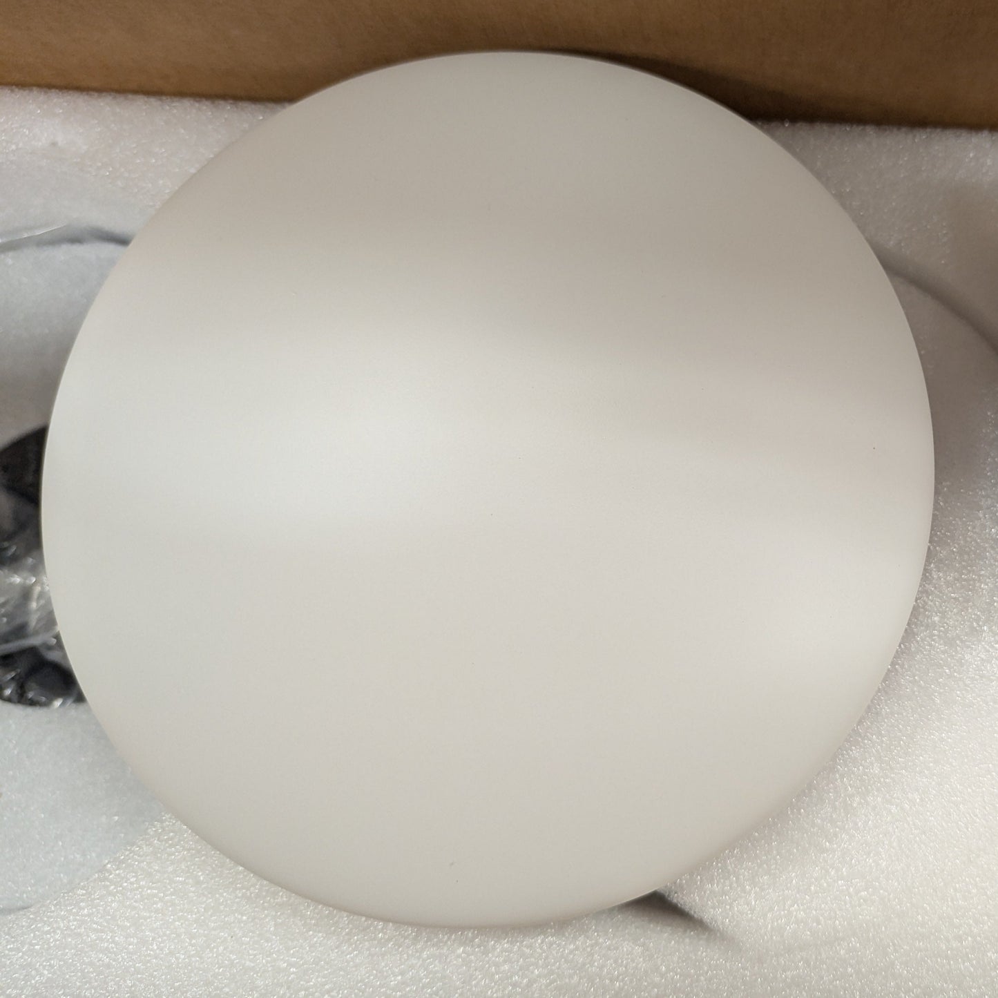 Round white light fixture with remote control on a beige surface