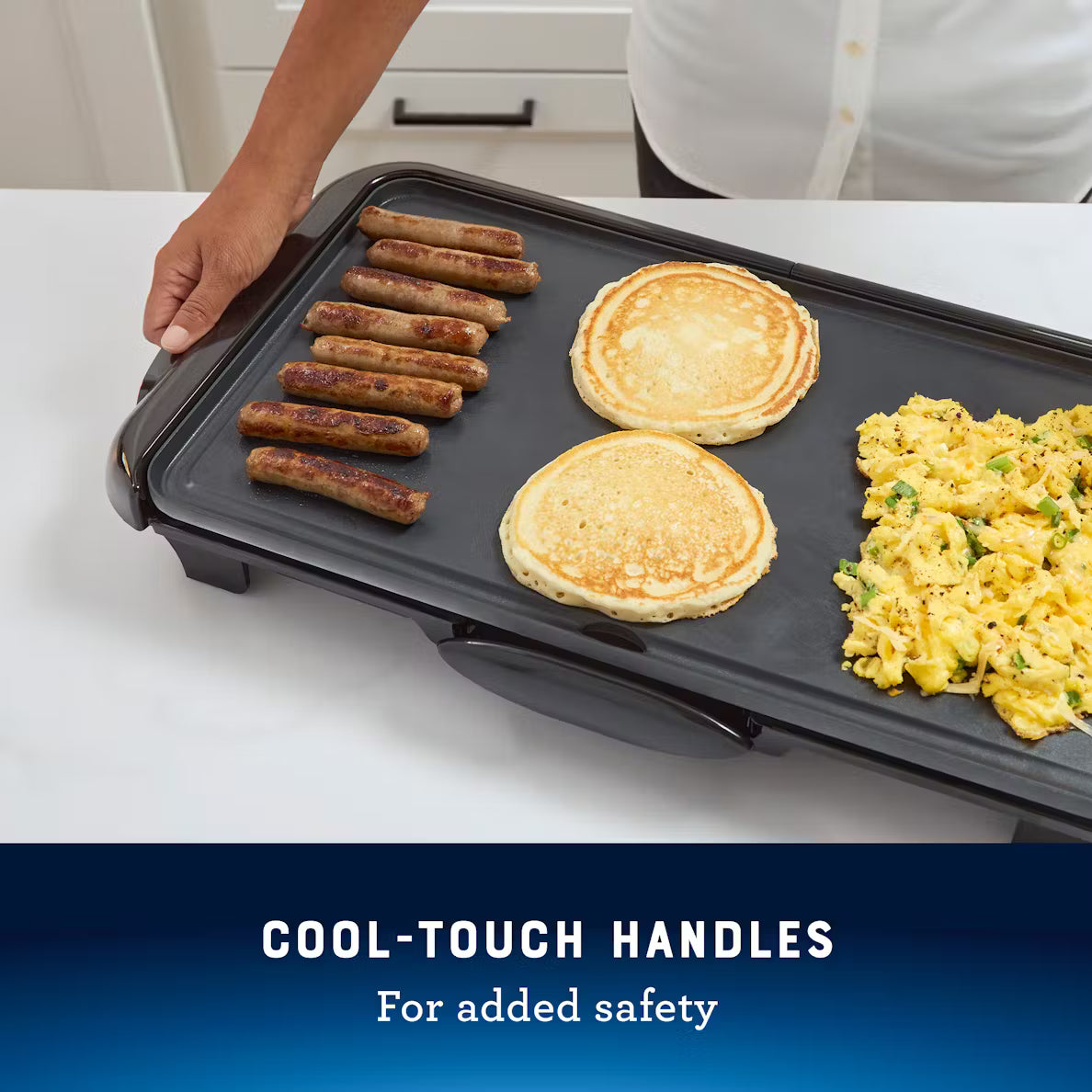 Electric griddle with pancakes, sausages, and eggs on a white surface with text 'Cool-Touch Handles for added safety'.