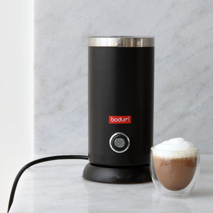 Black Bodum milk frother with a glass of frothed milk on a light gray background
