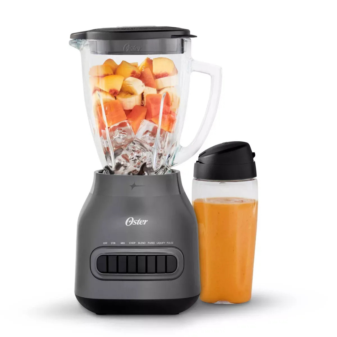 Oster blender with a container of chopped fruits and a glass filled with orange juice on a white background