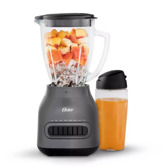 Oster blender with a container of chopped fruits and a glass filled with orange juice on a white background