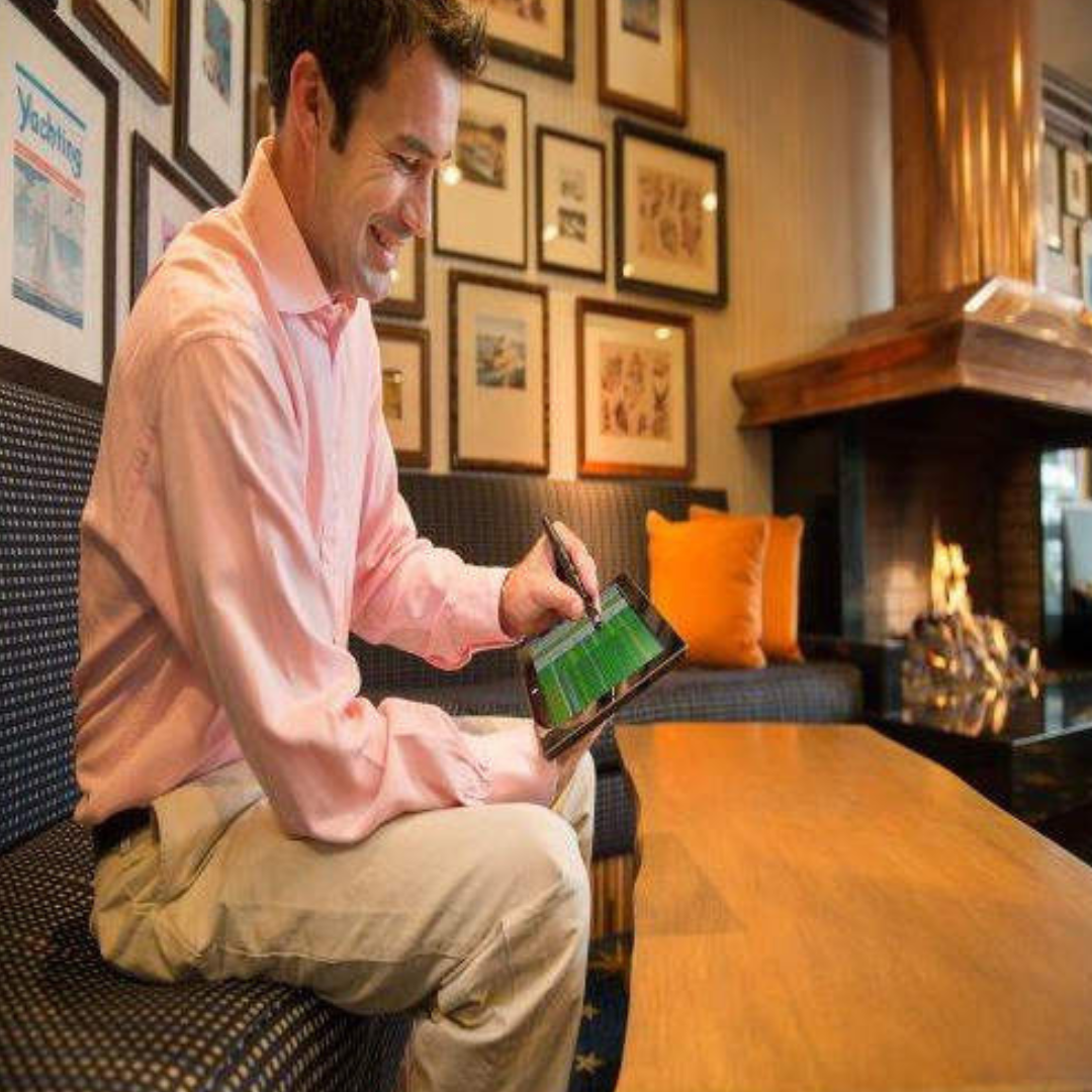 Man in a pink shirt using a tablet in a bar setting with framed pictures on the wall.