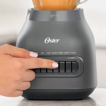 Oster blender with a hand pressing a button on a light background