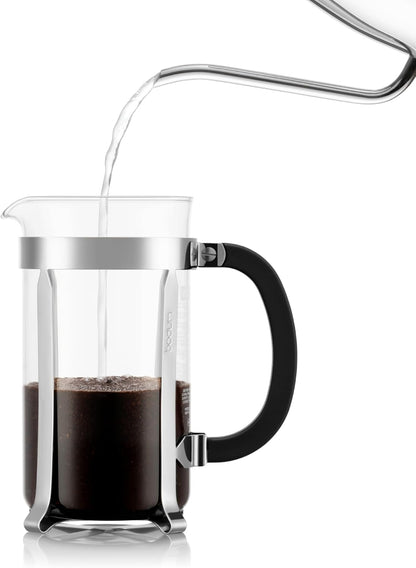 Glass French press with coffee being poured into it on a white background