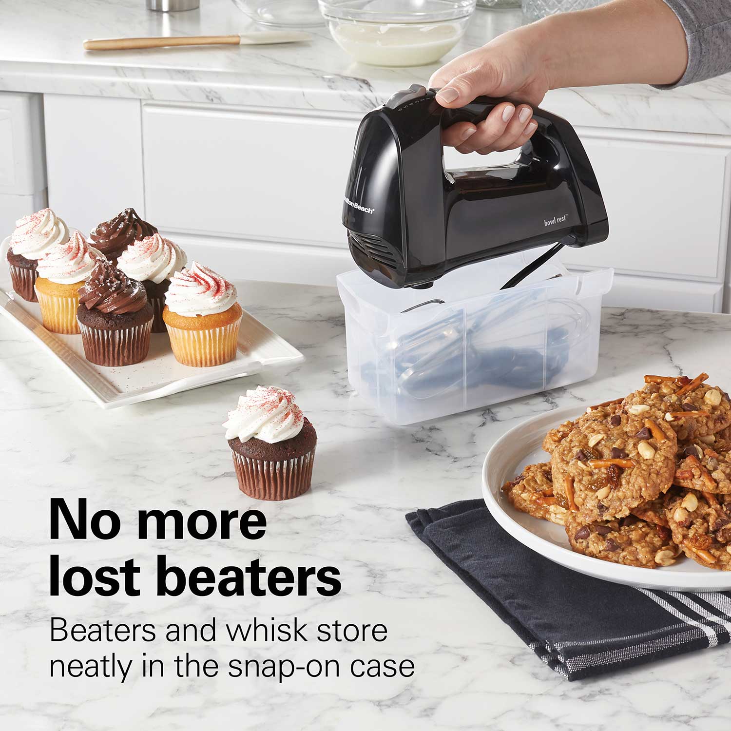 Hand mixer with snap-on case on a kitchen counter with baked goods.
