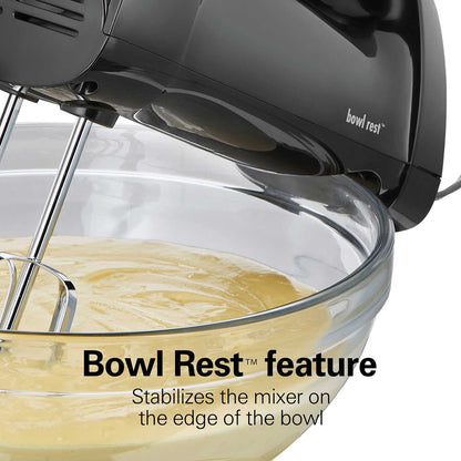 Black hand mixer with 'Bowl Rest' feature in action, mixing a yellow batter in a clear glass bowl.