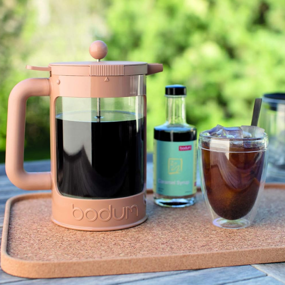 Bodum coffee press with iced coffee and a bottle on a wooden tray outdoors