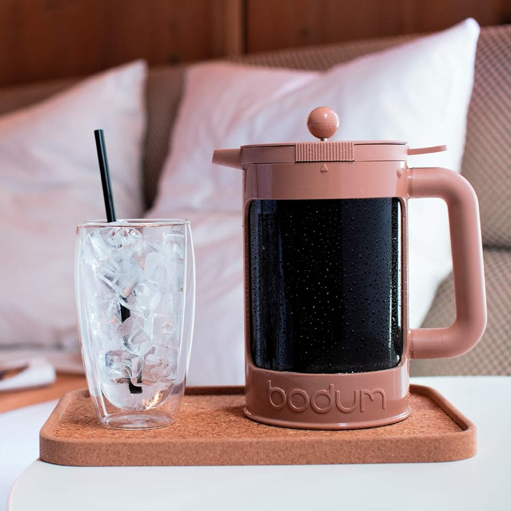 Bodum coffee press on a tray with a glass of iced coffee on a bed.