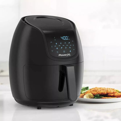 Black PowerXL air fryer on a white surface with a plate of food in the background