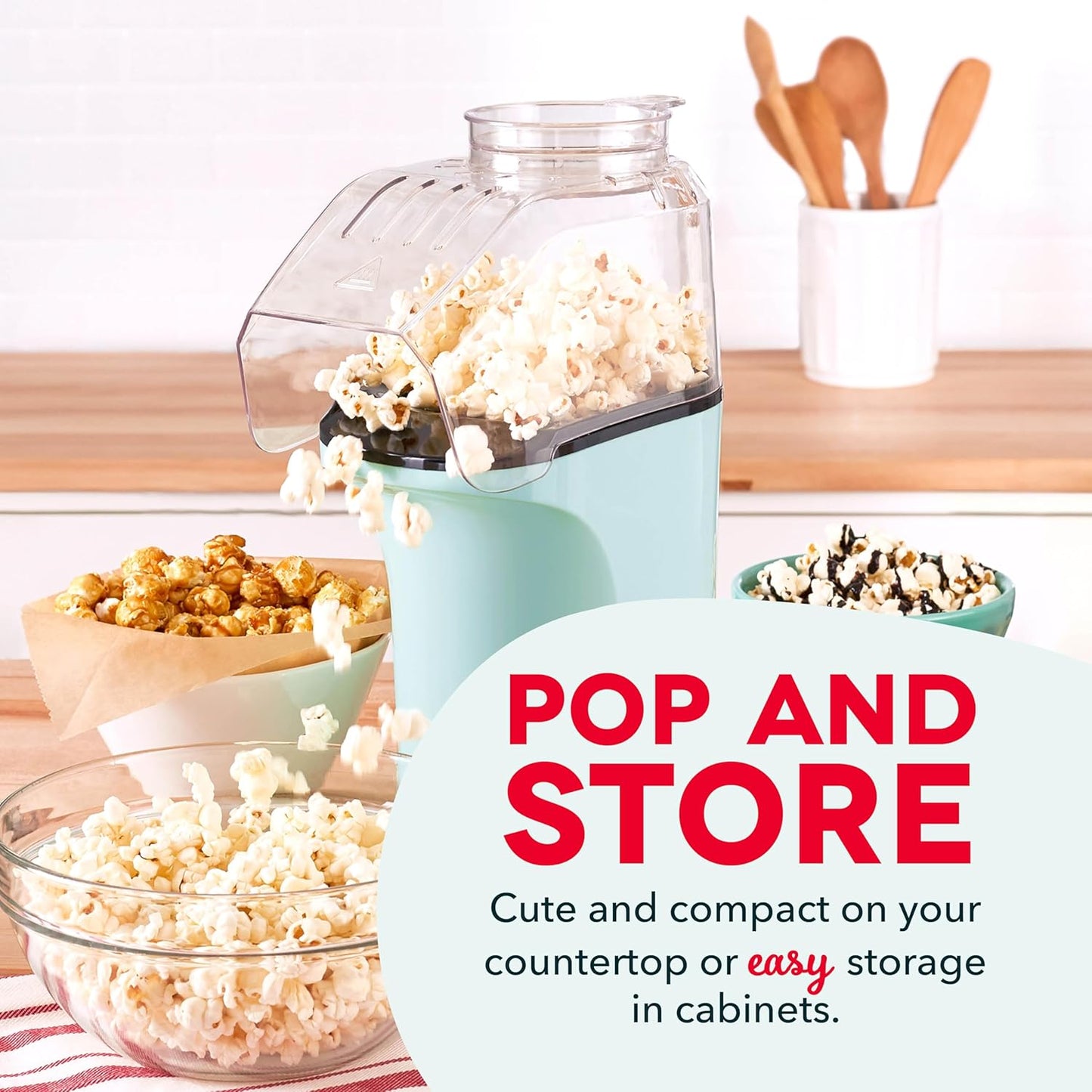 Popcorn maker with popped popcorn, bowls of popcorn, and kitchen utensils on a wooden surface.