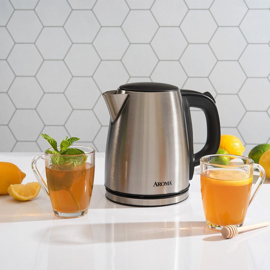 Stainless steel Aroma kettle on a kitchen counter with two glasses of juice and lemons.
