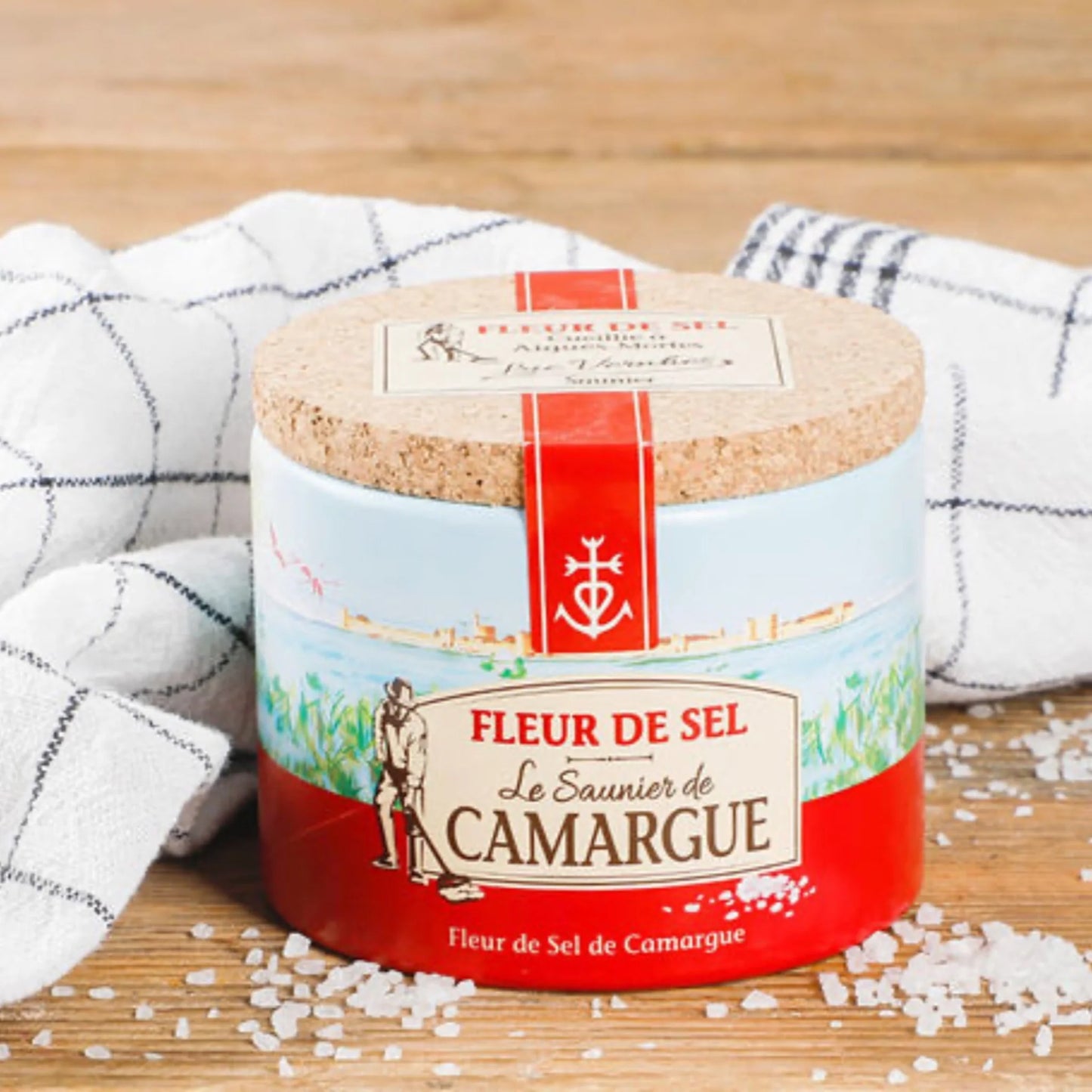 Container of Fleur de Sel from Le Saunier de Camargue on a wooden surface with salt crystals around.
