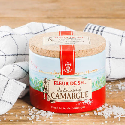 Container of Fleur de Sel from Le Saunier de Camargue on a wooden surface with salt crystals around.