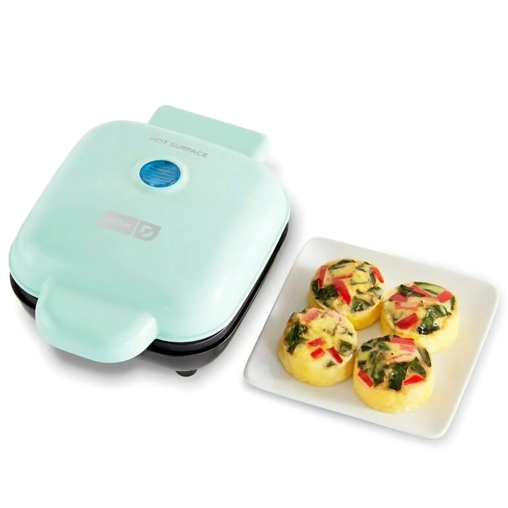 Mint green egg muffin maker with four egg muffins on a white plate.