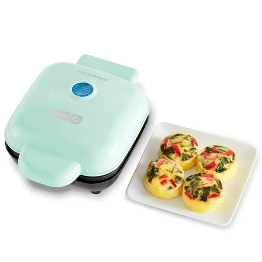 Mint green egg muffin maker with four egg muffins on a white plate.