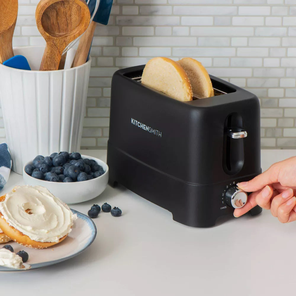 Black toaster with bread slices, bowl of blueberries, and plate of toast on a kitchen counter.