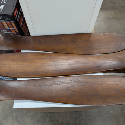 Three wooden shoe trees on a concrete floor with boxes in the background