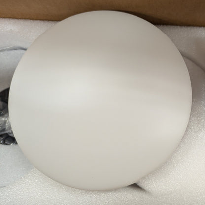 Round white light fixture with remote control on a beige surface