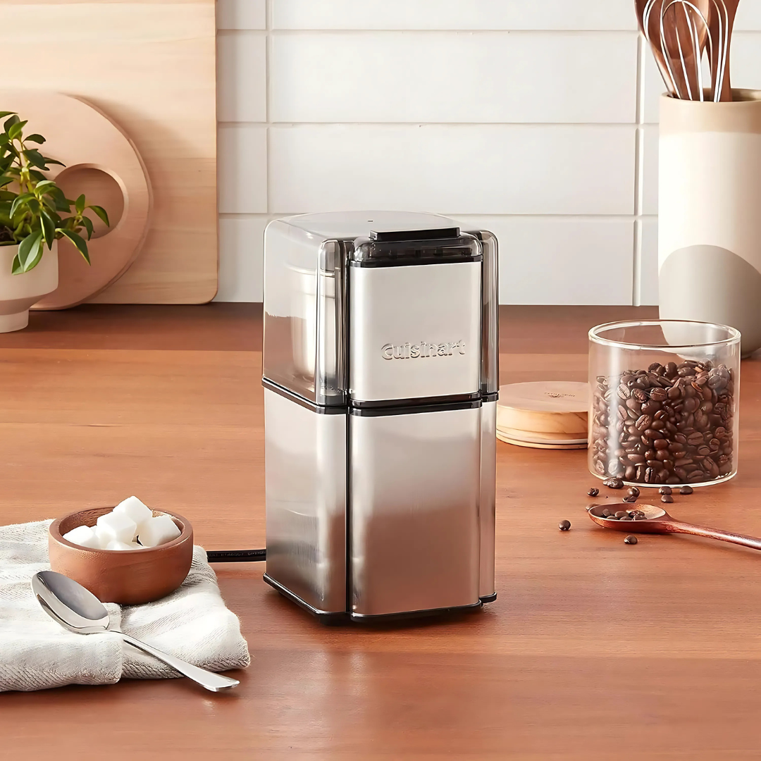 Coffee grinder on a kitchen counter with coffee beans and utensils in the background