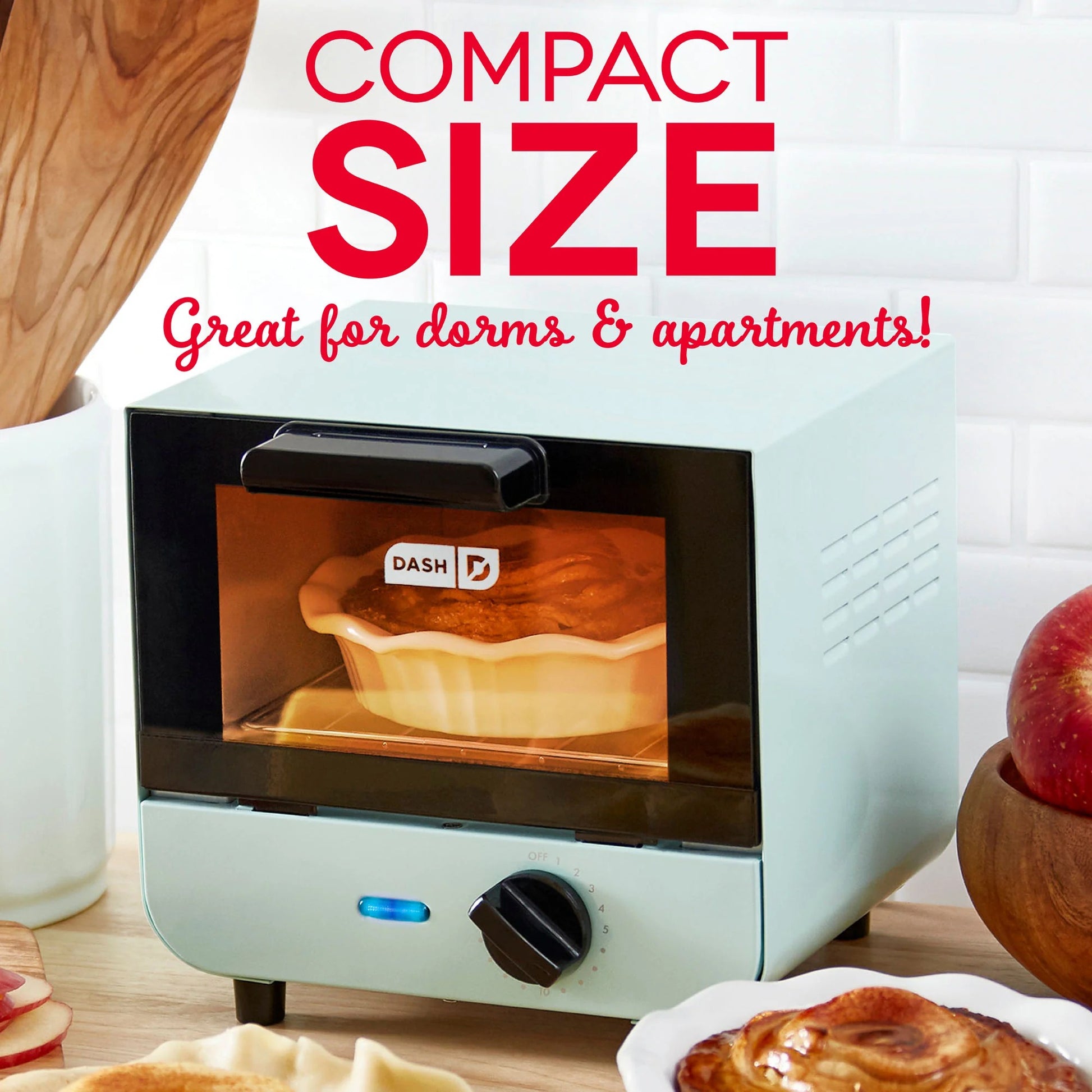 Small toaster oven with a pie inside, labeled 'Compact Size Great for dorms & apartments', on a kitchen counter.